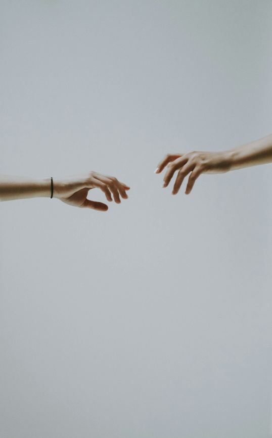 Two hands, almost touching, symbolizing the vital connection between therapist and client in trauma-informed therapy.