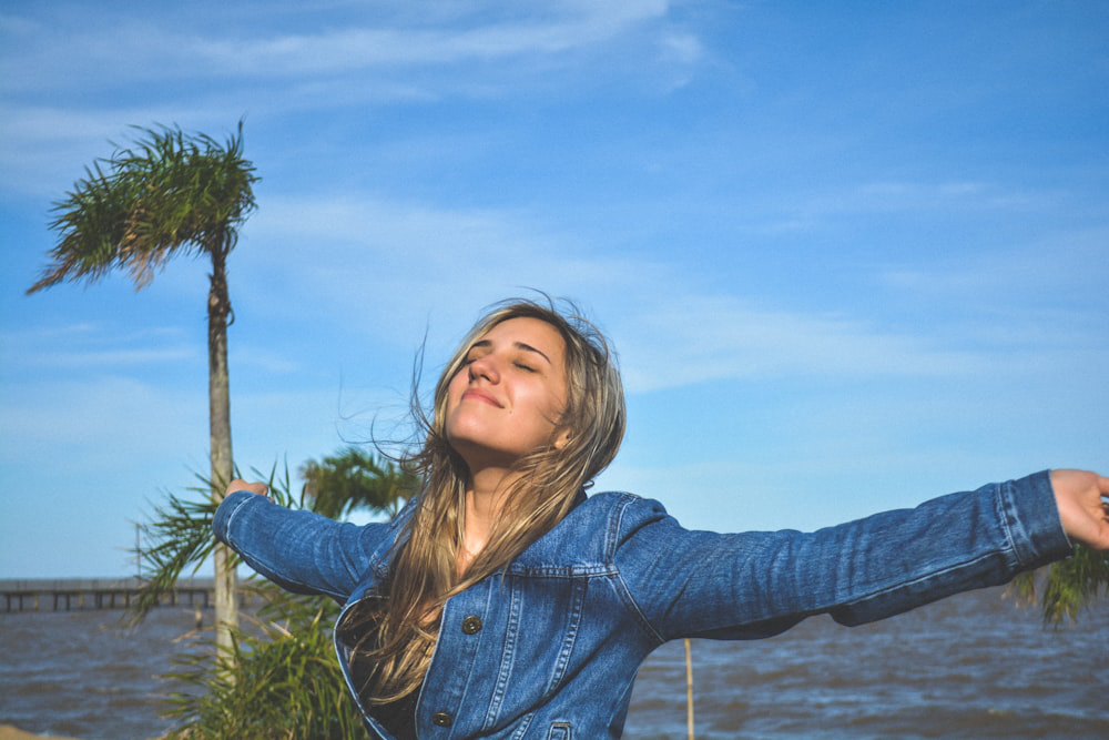 A woman with her arms outstretched and eyes closed, taking a deep breath and looking up at the sky.