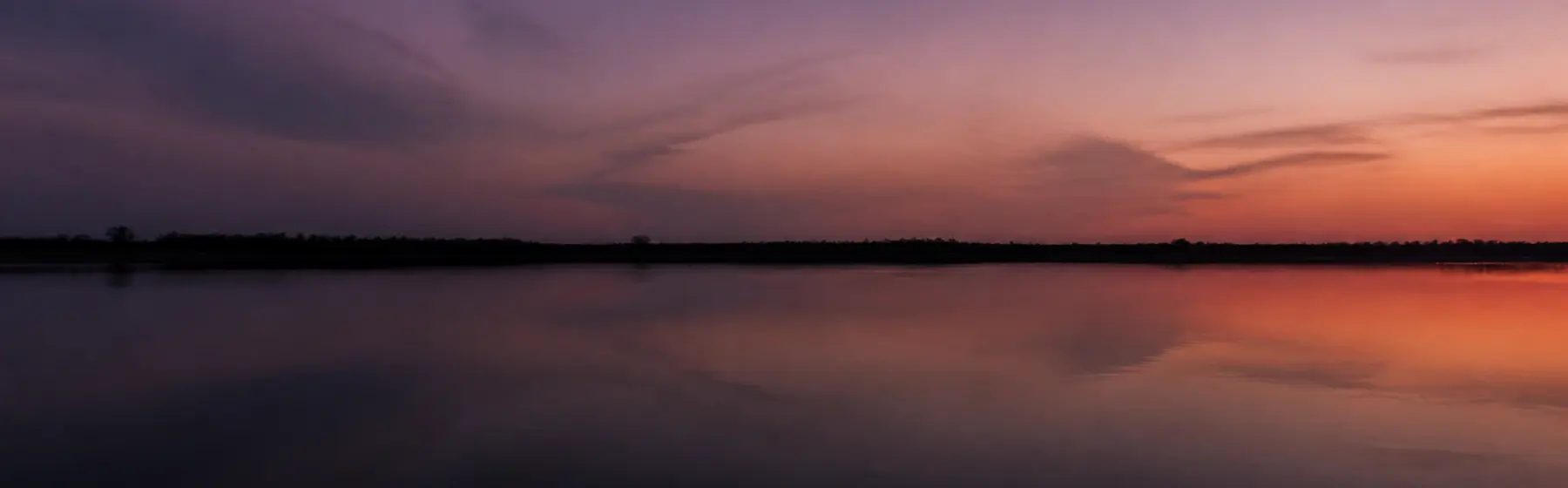 A still lake at dusk reflecting a violet and orange sky.