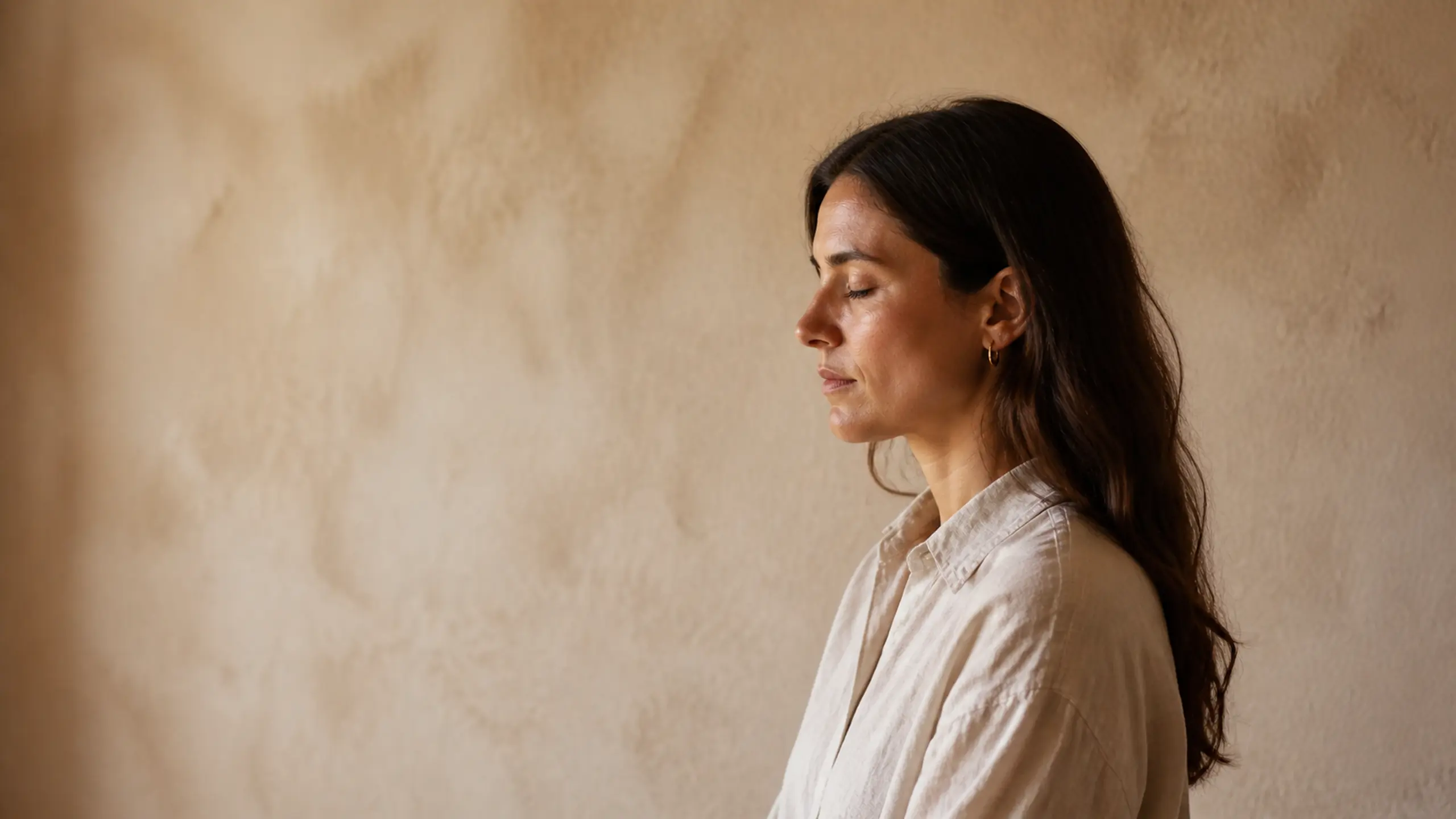 A woman standing in warm light with her eyes closed, breathing slowly.
